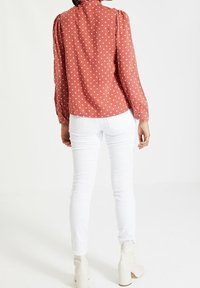 Rostfärgad blus med vita prickar, med puffärmar och hög halsringning, i kombination med vita skinny jeans och klackade ankelskotter.