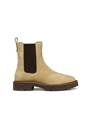 Bottine en suède beige avec un panneau élastique latéral marron, bout arrondi et semelle en caoutchouc. Inclut une languette à l'arrière pour un enfilage facile.