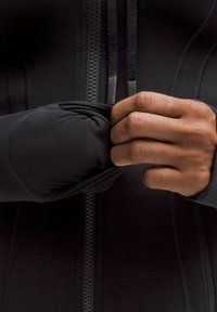 Fekete sportdzseki cipzárral, szoros ujjakkal, sima felülettel és rugalmas mandzsettákkal, amelyeket egy kéz állít be.