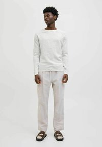 Maglietta grigia chiara a maniche lunghe, abbinata a pantaloni crema con tasche e sandali marroni con un accento di cinturino bianco. Design semplice.