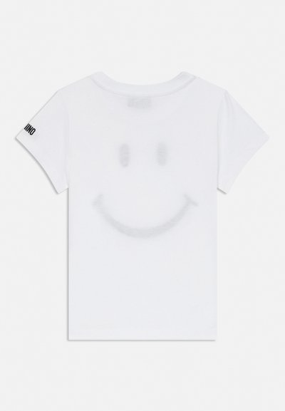 Bela majica s kratkimi rokavi s šibko veliko nasmejano obrazom spredaj in črnim besedilom na levem rokavu na belem ozadju.