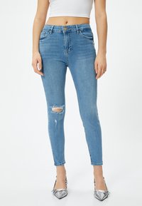 Tunna blå denimjeans med hög midja, med slitna knän och femficksdesign. Strukturerat tyg med lätt stretch.