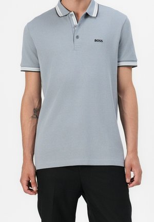 Mand iført lys grå polo med korte ærmer, hvid kant og "BOSS" logo på brystet, kombineret med sorte bukser.