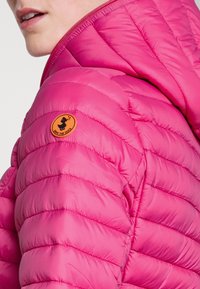 Giacca puffy fucsia con cappuccio, caratterizzata da un design trapuntato, una texture liscia e un logo rotondo arancione "Save the Duck" sulla spalla.