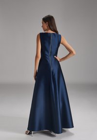 Navyblaue lange Abendgarderobe aus Satin, mit Rundhalsausschnitt, ärmellosem Design und sichtbarem Reißverschluss hinten. Glatte Textur und fließende Form.