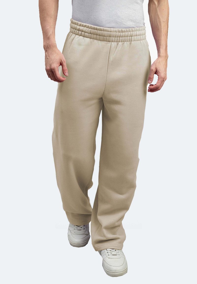 Beige Fleece-Hosen mit elastischem Bund, die eine lockere Passform und tapered Design aufweisen. Kombiniert mit weißen Sportschuhen.