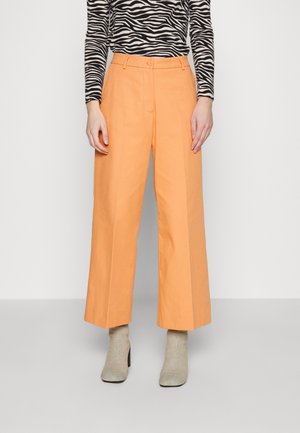 Mujer vistiendo pantalones melocotón de talle alto y pierna ancha combinados con calcetines con tacón beige y una blusa de manga larga con estampado de cebra en blanco y negro.