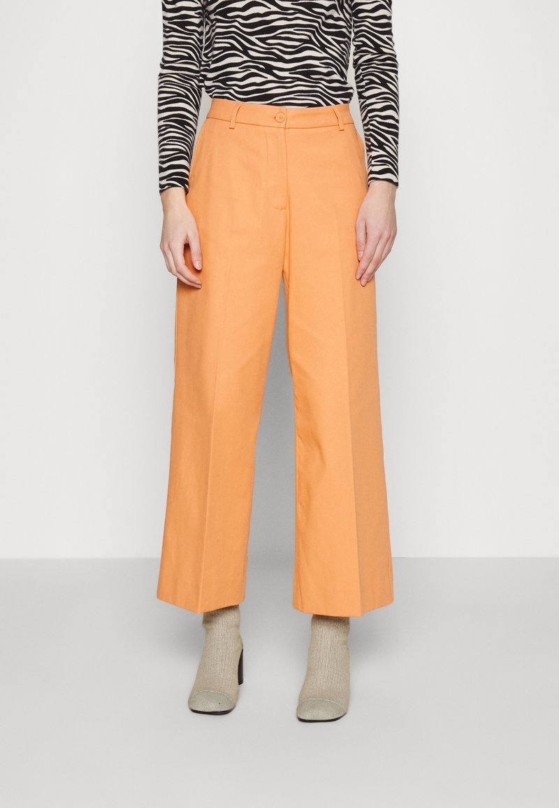 Femme portant un pantalon pêche taille haute à jambes larges, associé à des chaussettes beiges à talons et un top à manches longues imprimé zèbre noir et blanc.