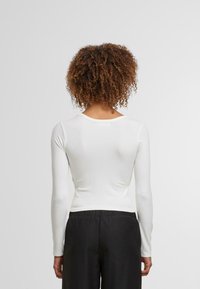 Witte lange mouwen top in ribbelstructuur, nauwsluitend, met een ronde halslijn. Gekoppeld aan zwarte, loszittende broek.