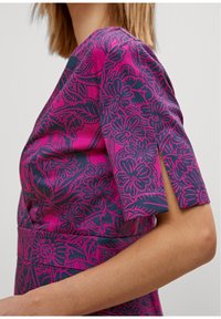 Abito a maniche corte con un vivace motivo floreale rosa su uno sfondo scuro. Il tessuto ha una texture liscia ed un design aderente.