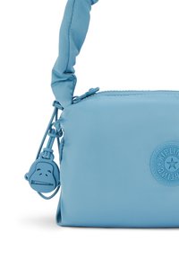 Ljusblå nylonhandväska med en strukturerad, vadderad rem, som har en cirkulär logotyp och en dragkedjepryl med en lekfull apa-design.
