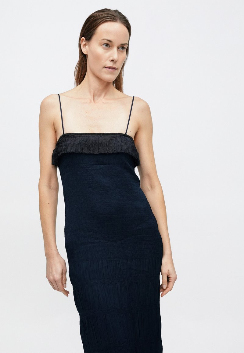 Mørkeblå kjole med en lige silhuet, med en frynset sort halsudskæring og tekstureret stof. Spaghettistropper fuldender designet.