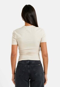 Camiseta de manga corta beige con un diseño ajustado y un escote redondo, combinada con jeans negros de cintura alta con bolsillos traseros.