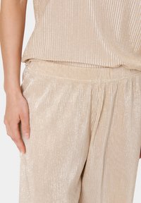 Beige ribbed knit top with matching elastic waistband pants, featuring a subtle shimmer and soft texture, highlighting a relaxed fit.