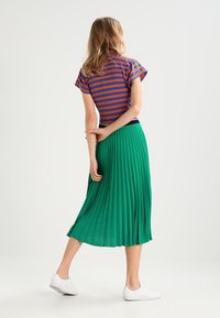 Camiseta a rayas en azul y naranja, falda midi plisada verde, combinada con zapatillas blancas; textura suave y diseño casual.