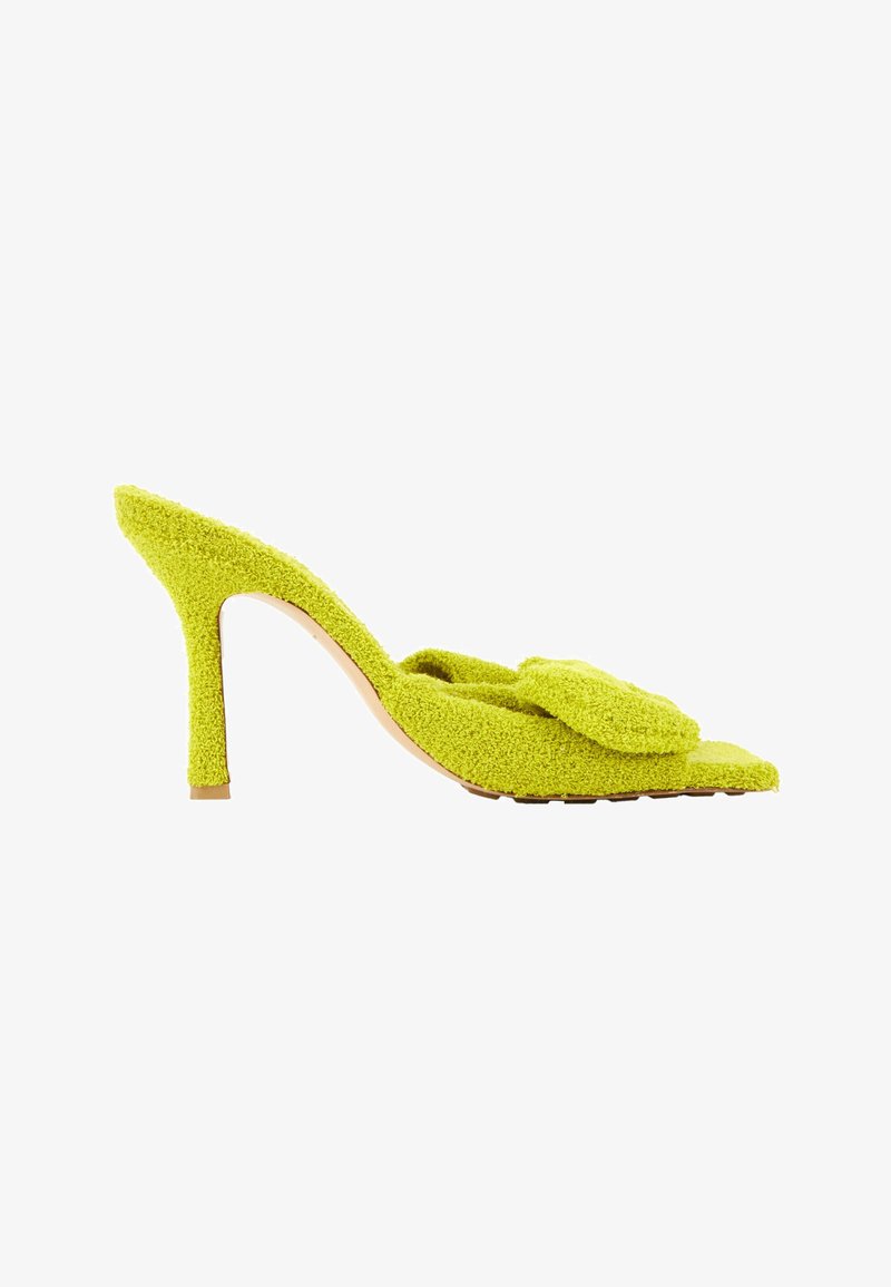 Mule verte texturée à talon haut avec un bout pointu et une bride décorative sur la partie supérieure de la chaussure.