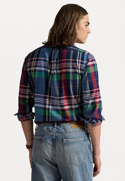 Daugiaspalvis langelių marškiniai, kuriuose yra mėlynų, raudonų, žalių ir geltonų kvadratų, su sukabintomis rankovėmis ir mygtukų apykakle, pagaminti iš medžiagos.