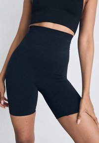 Høyt liv svarte sykkelshorts laget av elastisk stoff, med en glatt tekstur og sømmer, designet for komfort og passform.