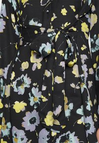 Vestido preto com padrão floral em amarelo, azul e lavanda, apresentando um cinto frontal de tecido atado em nó na cintura.