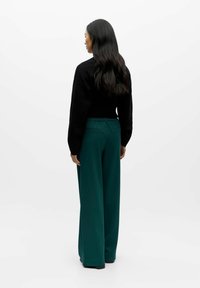 Black sweater and wide-leg green trousers. The pants feature a smooth texture and elastic waistband with back pockets.