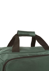 Bolsa de deporte de tela verde con asas de correa negra y cremallera. Forma cuadrada, superficie texturizada, costuras reforzadas y diseño minimalista.