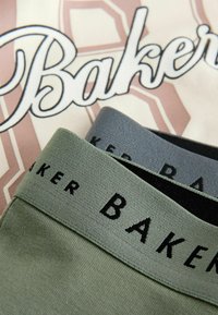 Zwei elastische Taillenbänder in Grün und Grau mit dem Text "BAKER", auf einem Hintergrund mit einem pinkfarbenen und weißen grafischen Design.