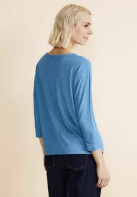 Maglione blu, morbido e leggero, con maniche a tre quarti. Tessuto soffice e scollatura tonda. Sul retro presenta un delicato dettaglio arricciato.