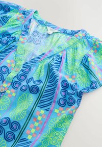 Chemise à motifs bleus avec des tourbillons et des designs floraux en vert vif, rose et bleu. Tissu doux avec un col en V et une fermeture à boutons.