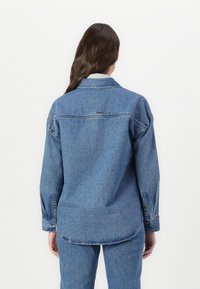 Camicia di jeans leggera di colore azzurro con vestibilità rilassata, polsini con bottone e colletto. Presenta un orlo dritto e dettagli di cucitura sottili.