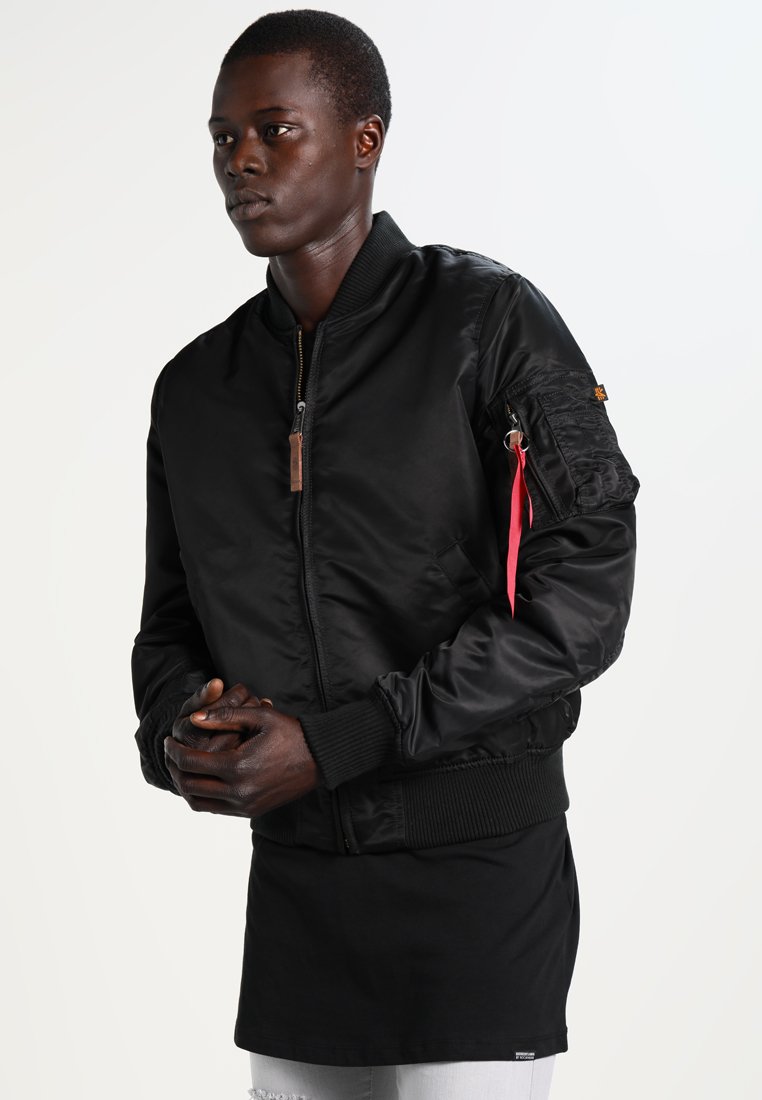 Veste bomber noire en tissu brillant, avec des poignets côtelés, un zip à l'avant et une poche avec une étiquette rouge sur la manche gauche.
