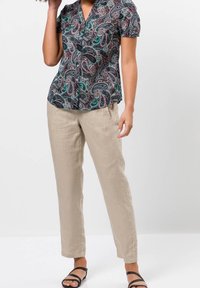 Blouse à manches courtes noire avec un motif paisley vert, rouge et blanc, accompagnée d'un pantalon en lin beige. Des sandales complètent la tenue.