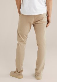 Pantalones de algodón beige con un ajuste slim, con bolsillos traseros y una textura suave. Combinados con zapatos de lona beige.