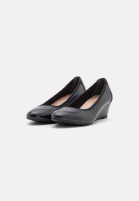 Chaussures compensées en cuir noir avec une finition lisse, des bouts pointus et un talon bas. Le design comprend une ouverture arrondie et un doublure intérieure douce.