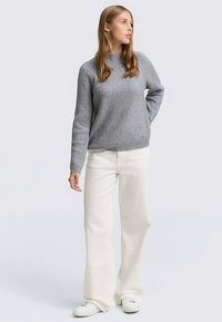 Szary sweter prążkowany z okrągłym dekoltem, w połączeniu z białymi szerokimi spodniami i białymi trampkami. Strój charakteryzuje się luźnym krojem i gładką fakturą.