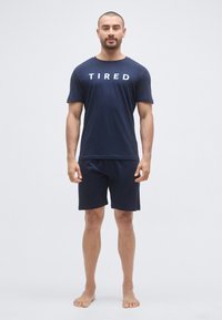 Μπλε βαμβακερό μπλουζάκι με το λευκό τύπωμα "TIRED", συνδυασμένο με ταιριαστά μπλε σορτς. Απλός σχεδιασμός, κοντά μανίκια και άνετη γραμμή.