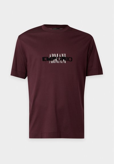 T-shirt manches courtes bordeaux foncé avec logo texte "Armani" superposé en noir et blanc au centre devant.
