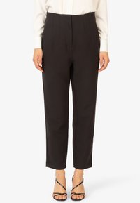 Schwarze maßgeschneiderte Hose mit hoher Taille, gefaltetem Vorderteil und geradem Bein. Hergestellt aus glattem Stoff und kombiniert mit schwarzen Riemchensandalen.