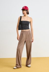 Black strapless top, loose tan pants, red baseball cap, black bag, white slip-on shoes. Soft textures and casual athletic style.