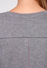 Grå bomull T-shirt med en enkel design, som har en horisontell söm över ryggen och kontrasterande röda sömdetaljer.