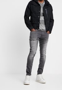 Černá džínová bunda se zipovou kapsou, šedé pruhované tričko, světlé šedé slim-fit džíny a bílé tenisky. Jednoduchý design s minimem detailů.