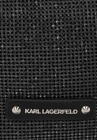 Juodas tekstūruotas audinys su apvaliais iškilimais. Yra juodas etiketė su sidabro spalvos užrašu "KARL LAGERFELD" ir dekoratyvine sidabro spalvos kniede.
