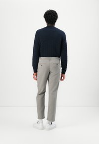 Navy textured knit sweater with a crew neckline, paired with light gray tailored trousers and white sneakers. Back view.