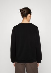 Sudadera negra de manga larga y cuello redondo, con una textura suave y dobladillo acanalado. Sin logotipos ni patrones visibles.