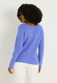 Suéter de punto color púrpura claro con textura acanalada, escote redondo y mangas largas, combinado con pantalones de color crema.