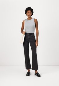 Grå ermeløs topp med en liten logo, høy midje svarte utsvingte jeans og svarte loafers. Hvit håndveske slengt over skulderen.