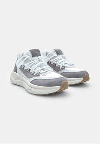 Un paio di sneakers grigie e bianche con suola spessa, lacci bianchi, occhielli metallici e morbida fodera in pelliccia su uno sfondo semplice.