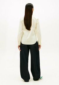 Langarmshirt met lichte gele strepen en een afgeronde zoom, gecombineerd met loszittende donkere spijkerbroek. Gladde stof, ontspannen pasvorm.