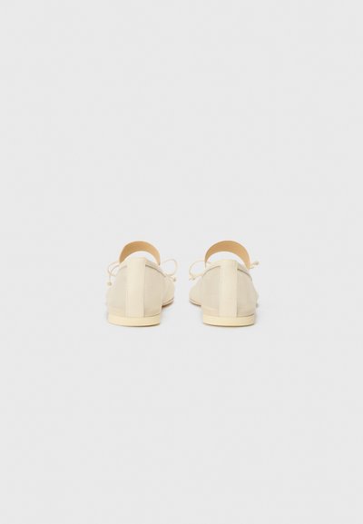 Beige flat shoes with a smooth, matte finish. Features a cut-out heel and tie closure with thin laces. Textured rubber sole.