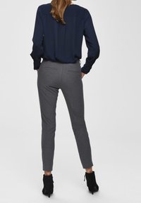 Grå skräddarsydda byxor med smal passform, med bakfickor och medelhög midja, parat med en marinblå blus. Svarta ankelstövlar fulländar looken.