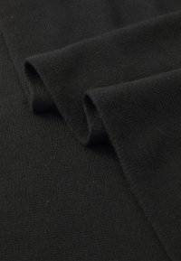 Svart stoff drapert i folder, med en teksturert strikket overflate. Materialet ser mykt og tett ut med en jevn farge gjennom hele.